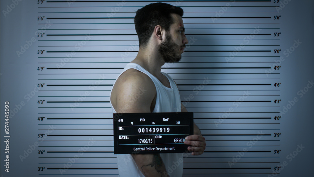 In a Police Station Arrested Beaten Man Poses for Side View Mugshot. He In a Police Station Arrested Beaten Man Poses for Side View Mugshot. He