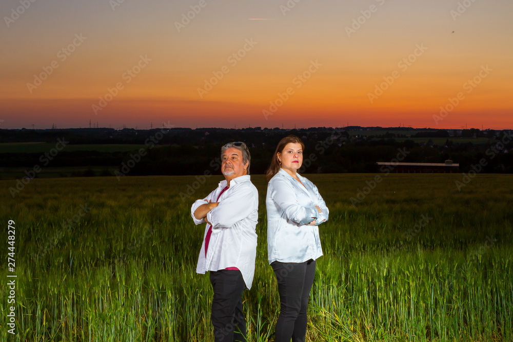 Man and woman stand putting their backs at each other as disagreement, at end of the day out in the field with the beautiful landscape that nature presents with the sunset. Man and woman stand putting their backs at each other as disagreement, at end of the day out in the field with the beautiful landscape that nature presents with the sunset.