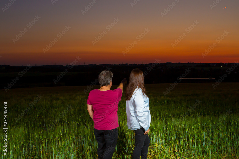 Couple standing together at end of the day out in the field looking at the beautiful landscape that nature presents with the sunset.