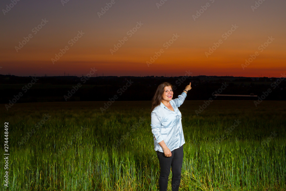 Lady standing at end of the day out in the field points at the beautiful landscape that nature presents with the sunset. Lady standing at end of the day out in the field points at the beautiful landscape that nature presents with the sunset.
