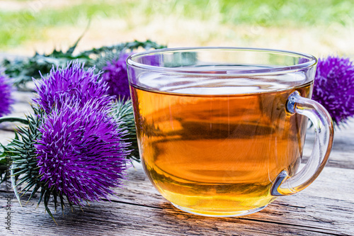 A cup of thistle tea on a woody background on nature. Thistle flowers near the cup with tea. Herbal tea. photo