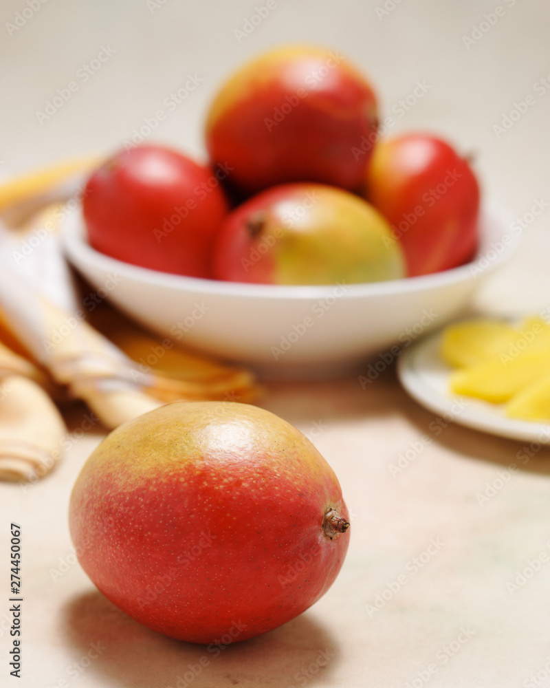 Delicious and healthy, ripe mangos in a bowl with plate of cut fruit on a softly colored table cloth Delicious and healthy, ripe mangos in a bowl with plate of cut fruit on a softly colored table cloth
