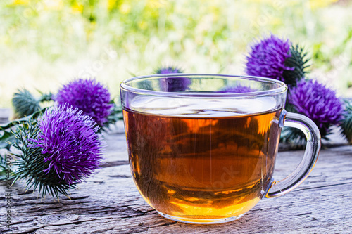 Tea with a thistle and flowers of a thistle medicinal plant on a wooden background. Pink thistle thistle flower. Herbal tea.