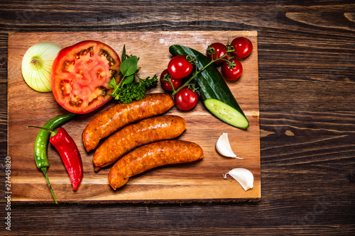 Raw sausages and vegetables on cutting board