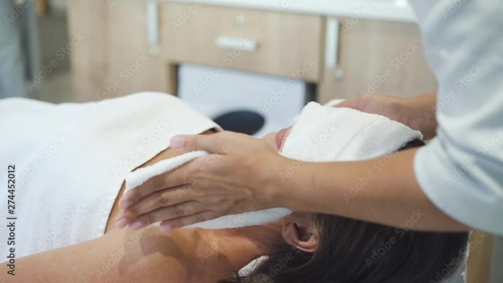 Cosmetology doctor putting towel to face of adult female customer. Woman lying on massage table during skincare procedure in spa salon. Slow motion. Cosmetology doctor putting towel to face of adult female customer. Woman lying on massage table during skincare procedure in spa salon. Slow motion.