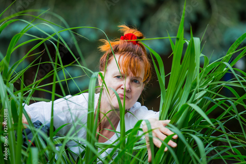 A curious woman is standing in a garden between plants and secretly observes. Concept curious neighbors. photo