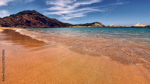 view from the sand of a menorca cove of crystal clear turquoise water.