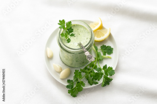 Papier peint Yoghurt cilantro sauce with garlic and olive oil in a glass jar on a white backg
