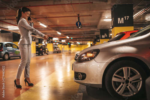 Elegant businesswoman locking her car with keys in underground parking..