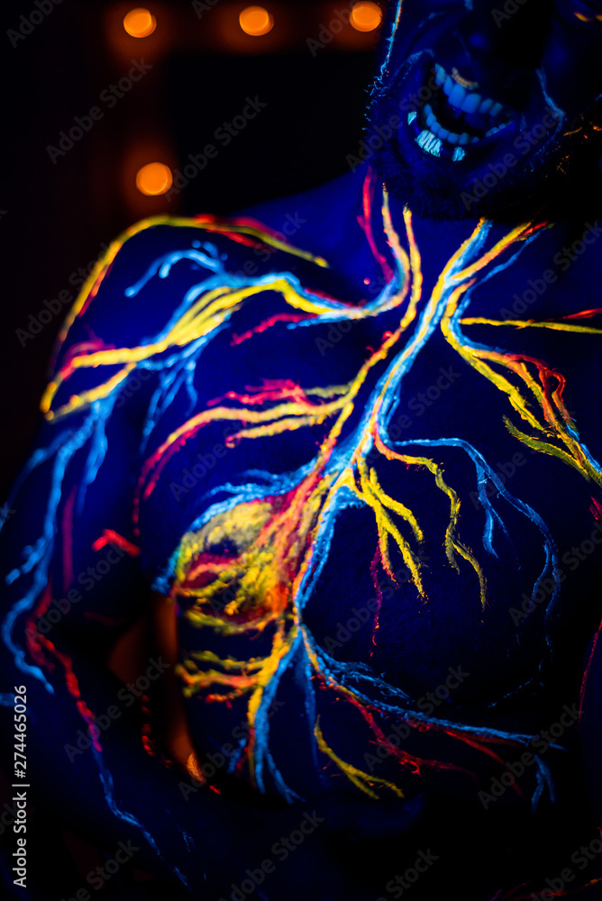 Obraz premium UV patterns body art of the circulatory system on a man's body. On the torso of a muscular athlete, veins and arteries are drawn with fluorescent dyes. Bodybuilder standing by the mirror with lamps.