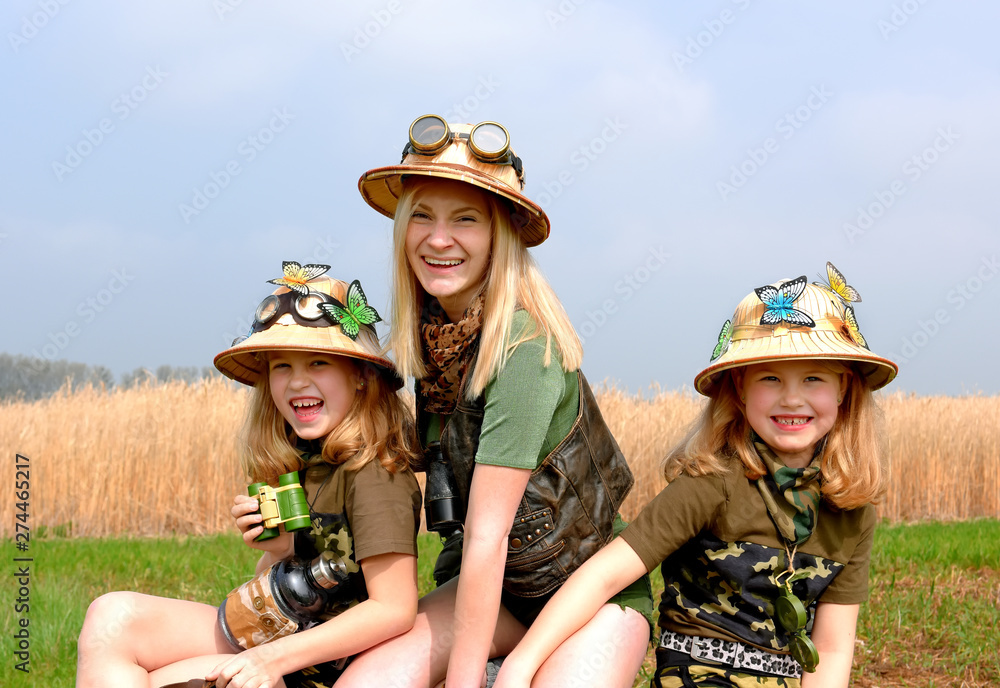 Twin young sisters and an adult girl dress up as explorers. They pose in  the outdoors