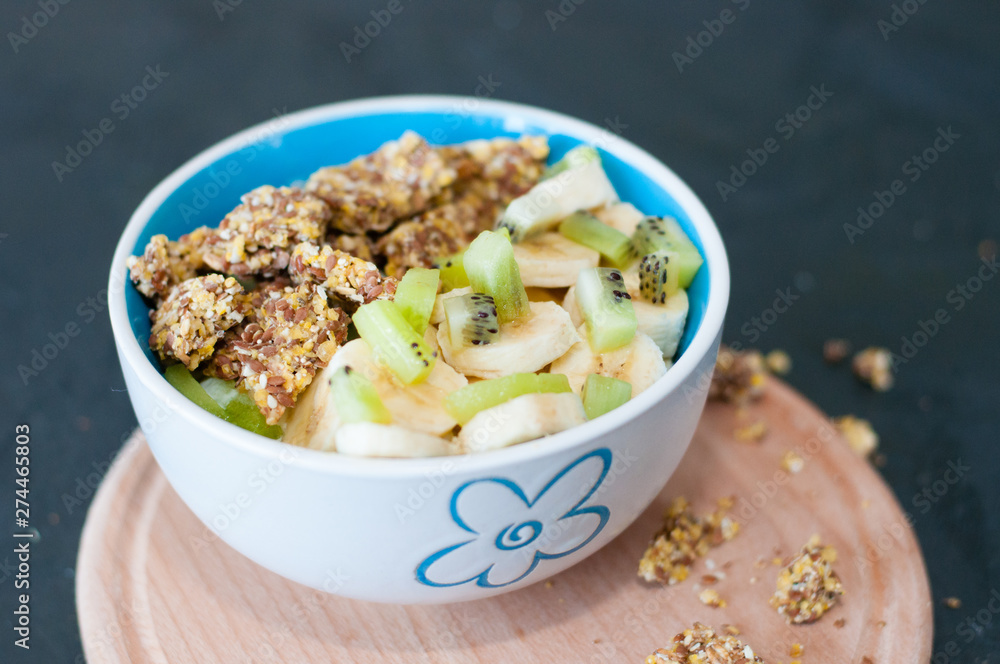 Granola, kiwi, banana and yogurt in a bowl on a wooden stand, dark background. Fitness diet for weight loss and proper nutrition Granola, kiwi, banana and yogurt in a bowl on a wooden stand, dark background. Fitness diet for weight loss and proper nutrition