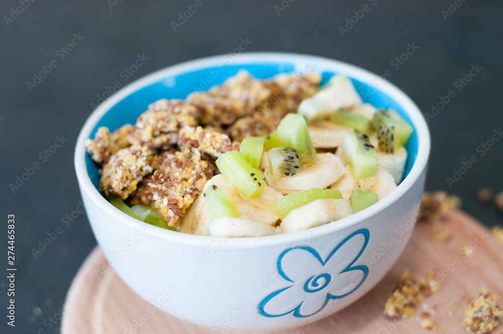 Granola, kiwi, banana and yogurt in a bowl on a wooden stand, dark background. Fitness diet for weight loss and proper nutrition Granola, kiwi, banana and yogurt in a bowl on a wooden stand, dark background. Fitness diet for weight loss and proper nutrition