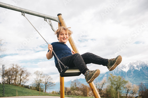 Kid boy having fun on swing in swiss alps, playground with beautiful view