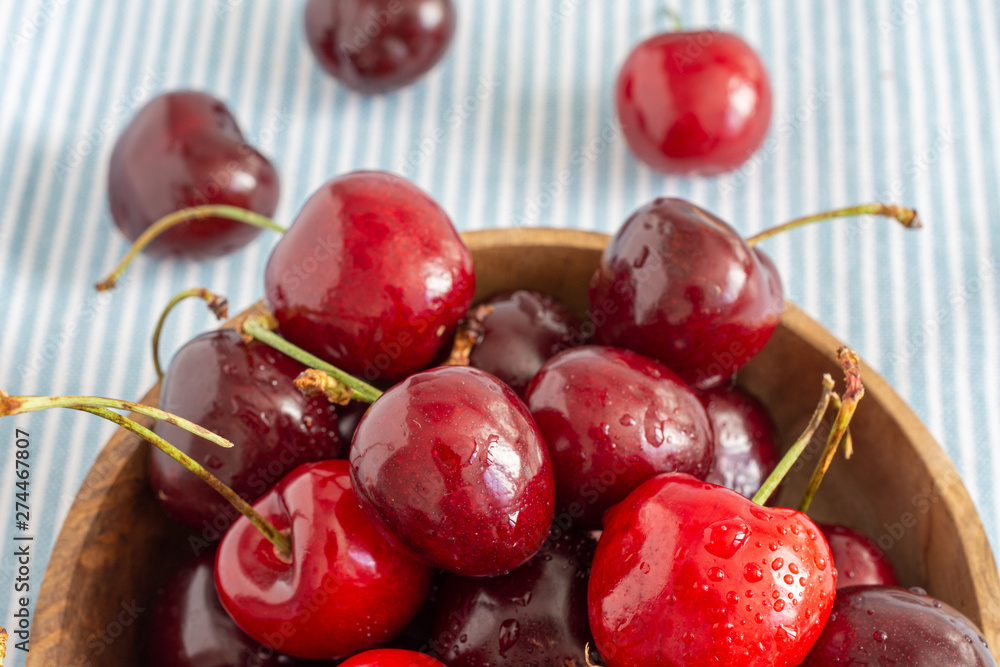 Top view of fresh cherries in wooden bowl on blue and white striped tablecloth Top view of fresh cherries in wooden bowl on blue and white striped tablecloth