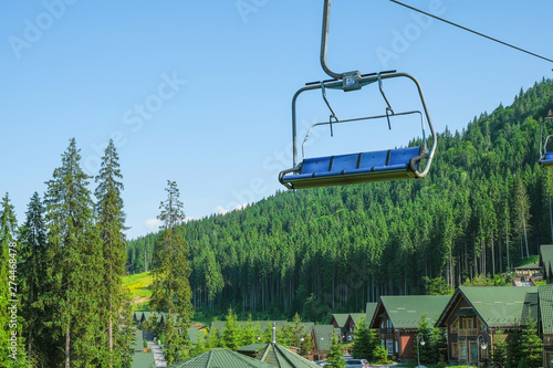 Scenic Lift Rides in the Carpathian Mountains in Ukraine. In the valley there are wooden houses with green roofs. Empty chair of the cable car.