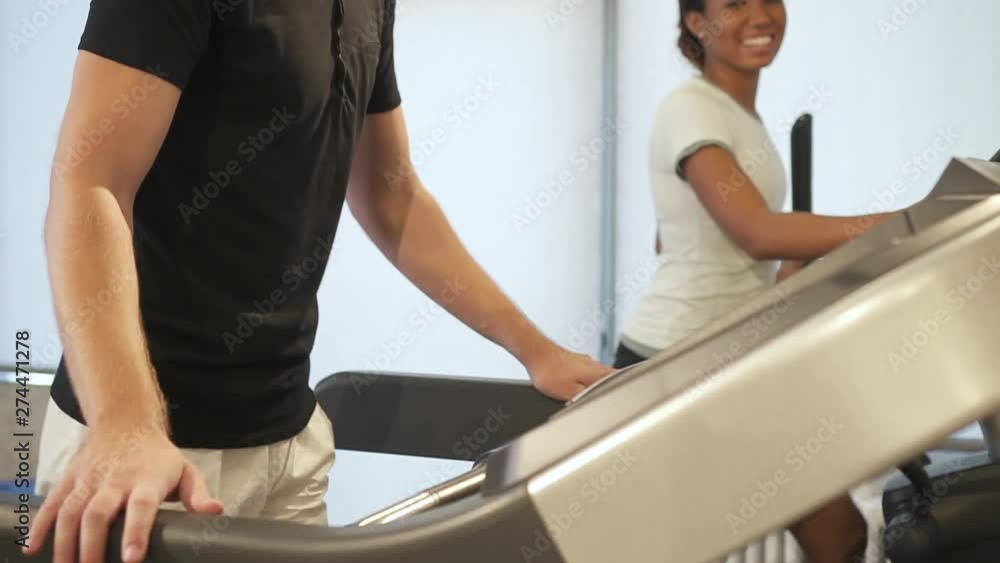 Cropped view of man on ready running on treadmill inside gym with light interior. He select or start workout program for cardio training against glad, sweet and positive young lady in good shape Cropped view of man on ready running on treadmill inside gym with light interior. He select or start workout program for cardio training against glad, sweet and positive young lady in good shape