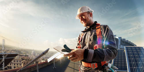 Solar energy engineer using tablet for check power station smiling in roof photo