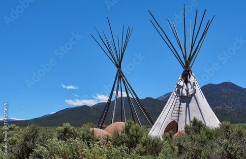 two tepees, one without skin, showing the poles