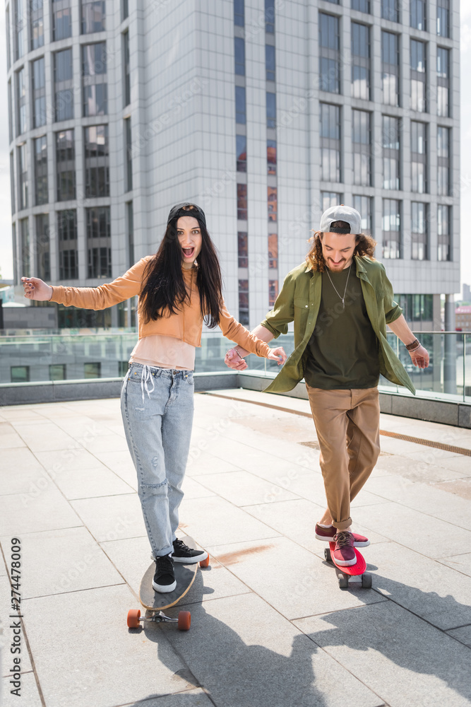 excited woman with happy man riding on skateboards on roof