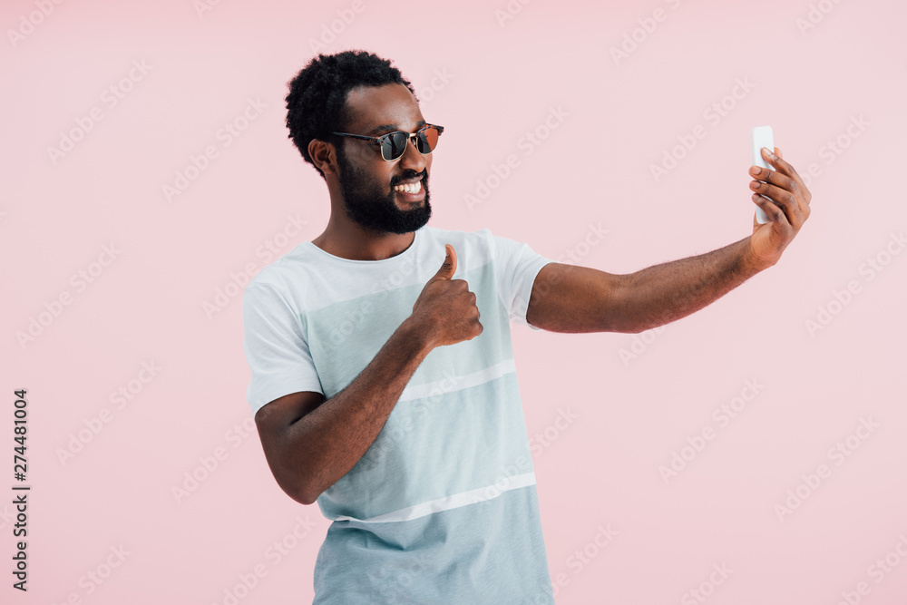 african american man in sunglasses with thumb up taking selfie on smartphone, isolated on pink african american man in sunglasses with thumb up taking selfie on smartphone, isolated on pink
