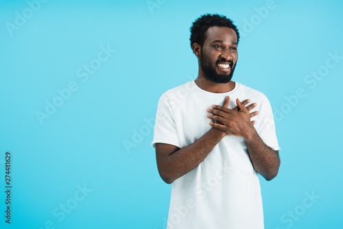cheerful african american man holding hands on heart isolated on blue