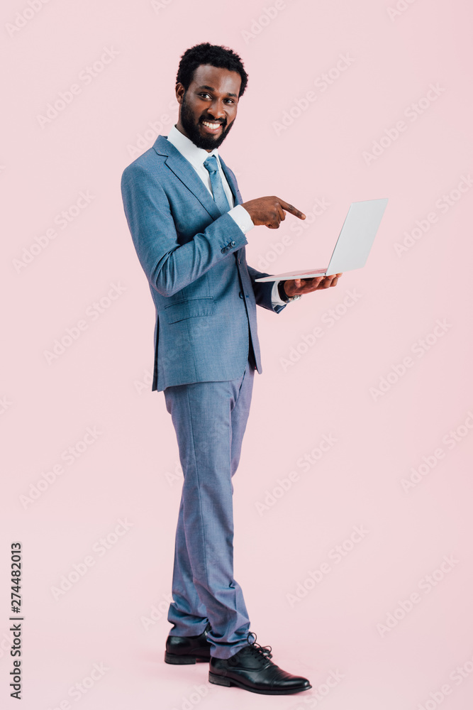 smiling african american businessman pointing at laptop isolated on pink smiling african american businessman pointing at laptop isolated on pink