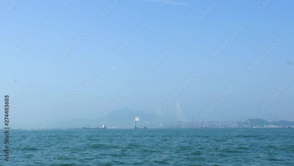 Ships floating on blue sea on car bridge and cityscape background. Commercial ships and boats swimming in sea. Mountain and industrial shipyard in distance. Hong Kong city panorama. Chinese city. Ships floating on blue sea on car bridge and cityscape background. Commercial ships and boats swimming in sea. Mountain and industrial shipyard in distance. Hong Kong city panorama. Chinese city.