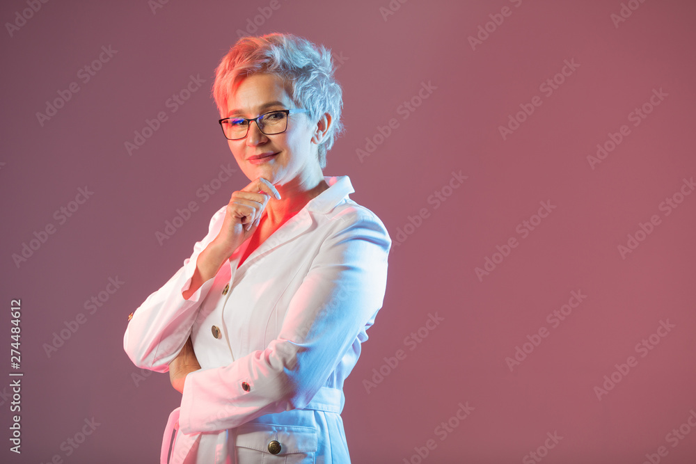 beautiful stylish woman aged, wearing glasses, in a white jacket on a pink background beautiful stylish woman aged, wearing glasses, in a white jacket on a pink background