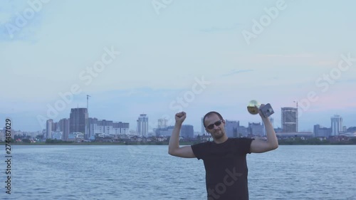 A young man with a cup in his hands rejoices in sports victory on background of the evening Minsk. Concept as victory, success and champion in sport. Slow motion. European Olympic Games in Minsk 2019.