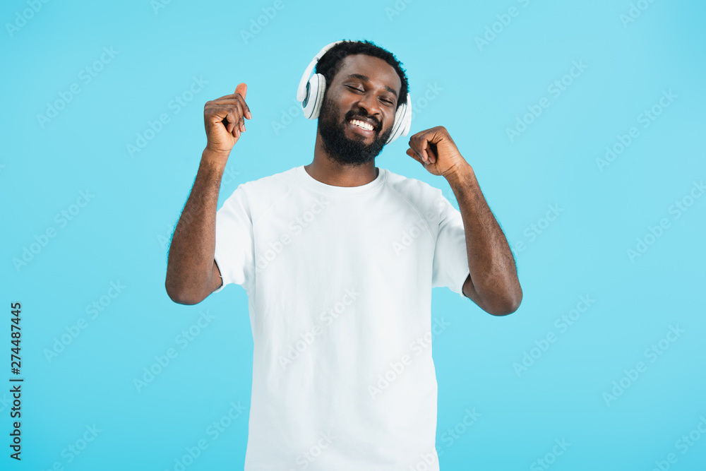 smiling african american man with closed eyes dancing and listening music with headphones, isolated on blue smiling african american man with closed eyes dancing and listening music with headphones, isolated on blue
