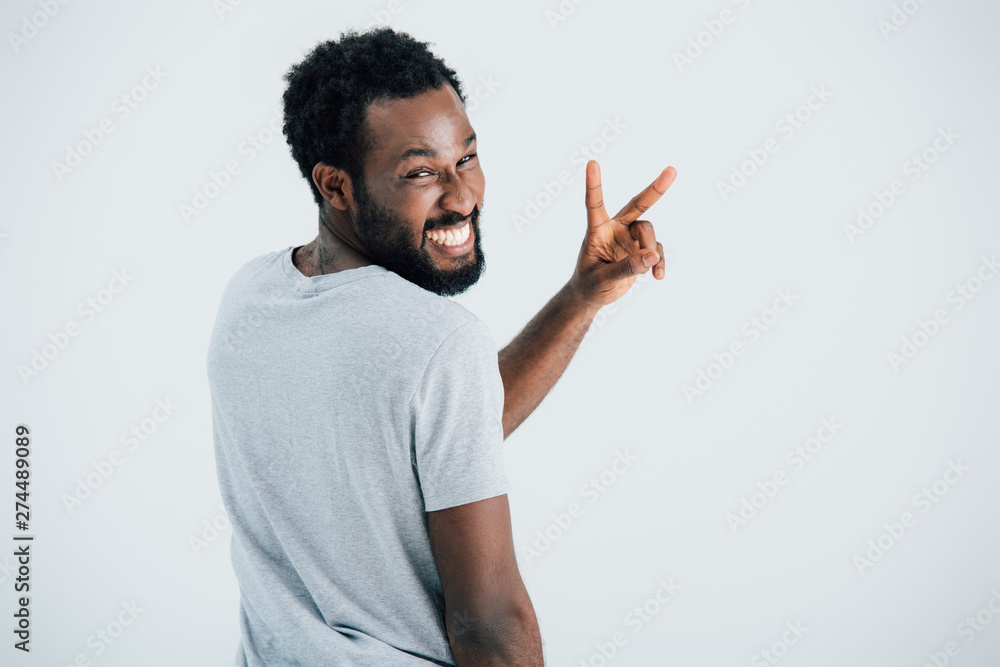 happy african american man in grey t-shirt showing victory sign isolated on grey happy african american man in grey t-shirt showing victory sign isolated on grey