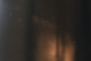 Flying dust at home in the sun on a background of dark curtains.
