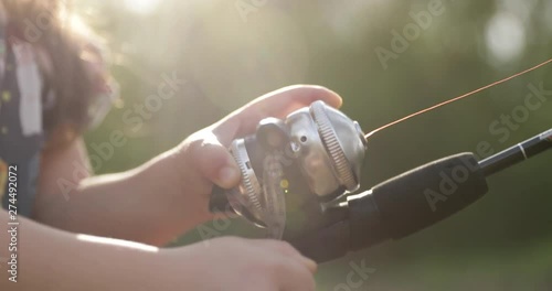 Close up of a child's hands reeling in fish on fishing pole in beautiful golden light with father.