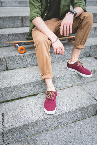 Cropped view of man sitting on skateboard at stairs
