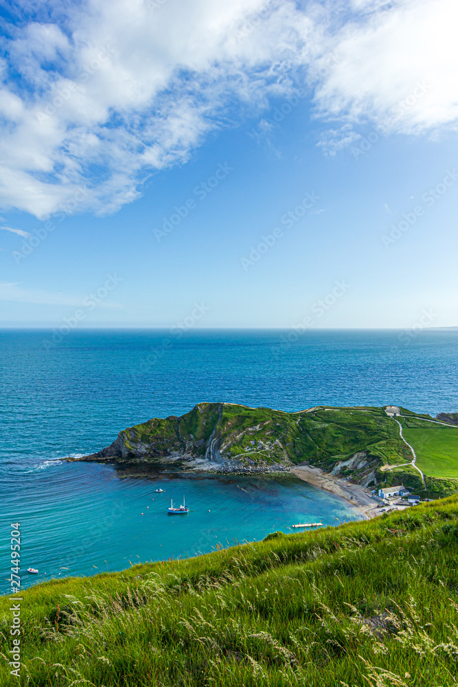 A view of the Lulworth Cove along the Jurrassic Coast in Dorset under a majestic blue sky and some white clouds. A view of the Lulworth Cove along the Jurrassic Coast in Dorset under a majestic blue sky and some white clouds.