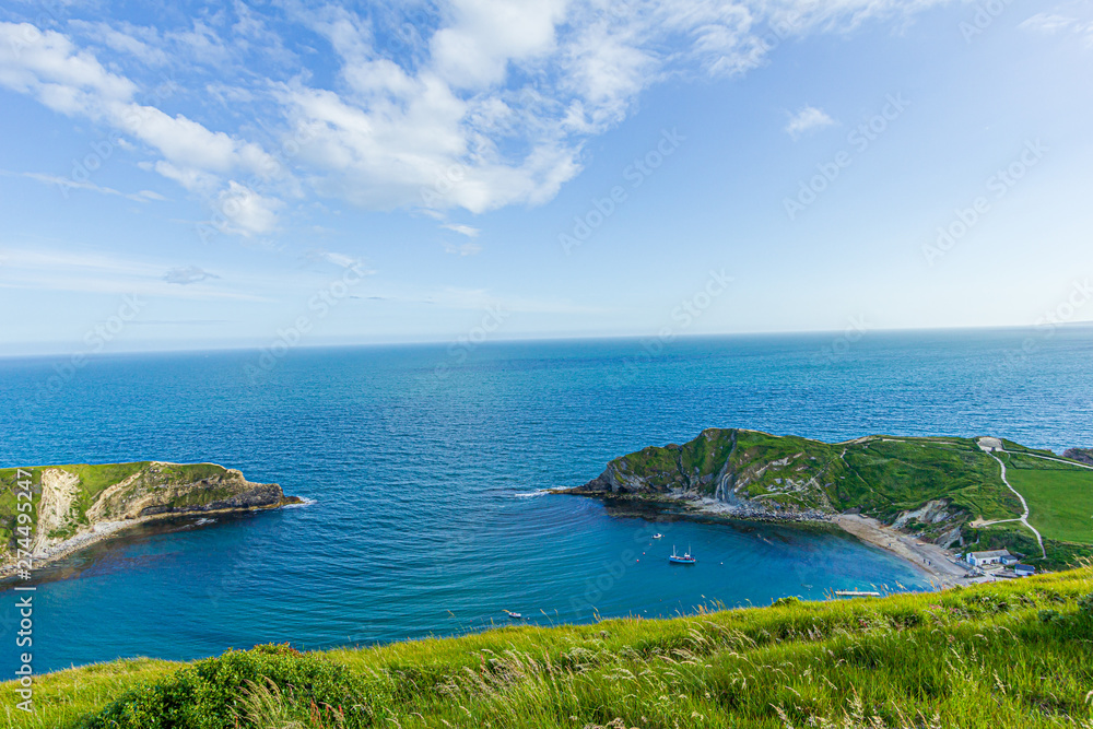 A view of the Lulworth Cove along the Jurrassic Coast in Dorset under a majestic blue sky and some white clouds.