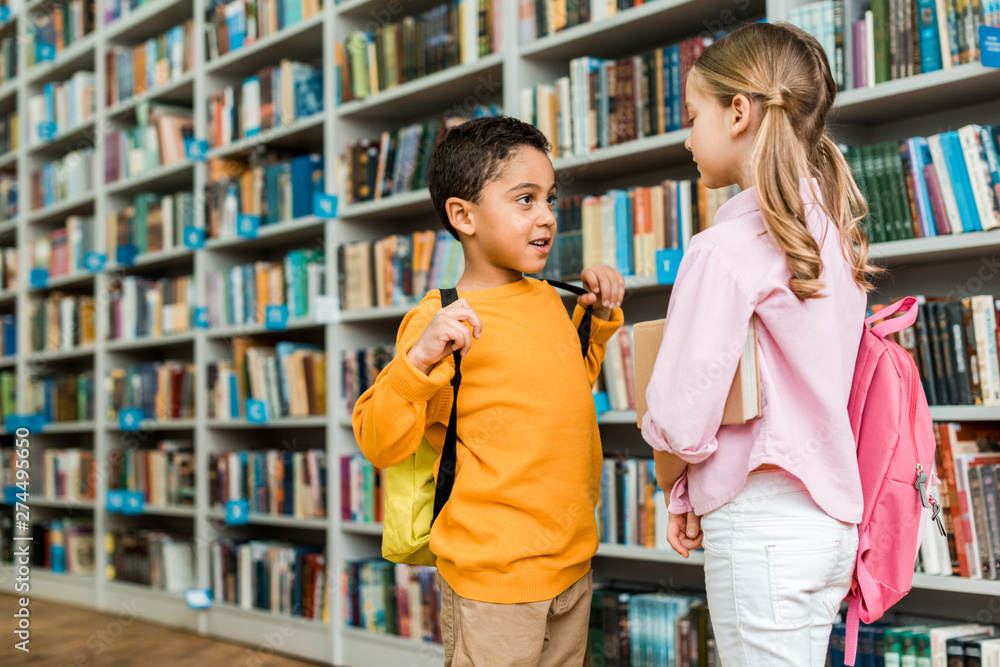 cute multicultural kids standing and talking in library cute multicultural kids standing and talking in library