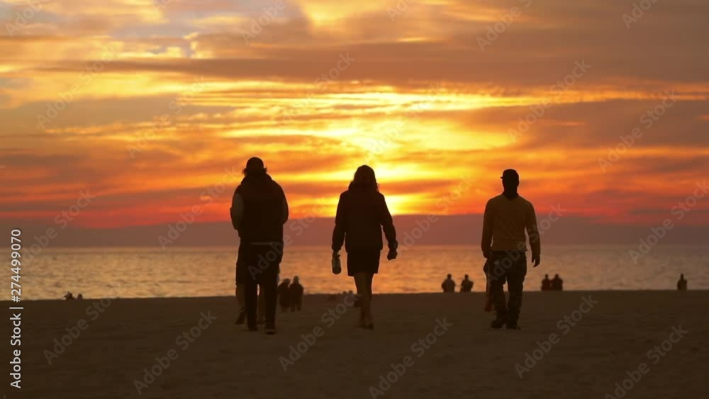 VENICE BEACH, SANTA MONICA, LOS ANGELES, California. People watching sunset by the ocean. Youth and adults on the sandy beach enjoy golden hour. VENICE BEACH, SANTA MONICA, LOS ANGELES, California. People watching sunset by the ocean. Youth and adults on the sandy beach enjoy golden hour.
