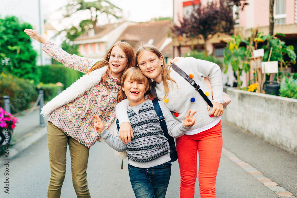 Φωτογραφία Group of 3 funny kids with backpacks, 2 schoolgirls and one preschooler, back to