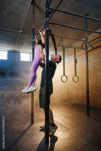 Personal trainer helping handsome sport woman doing pull up exercise in the gym.