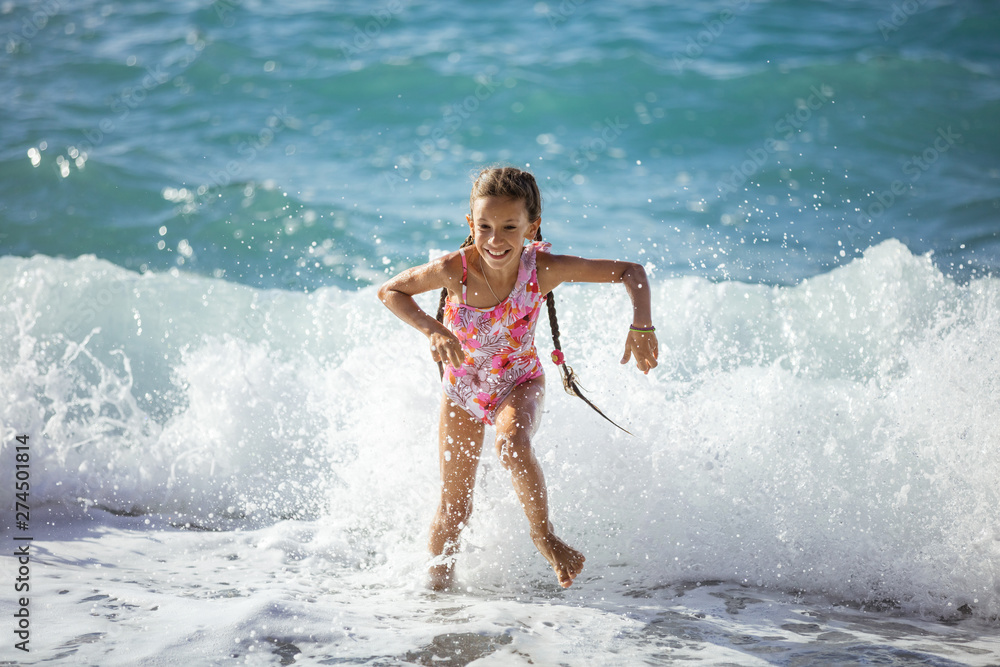 Fototapeta premium Happy young girl playing on beach and running away from big waves