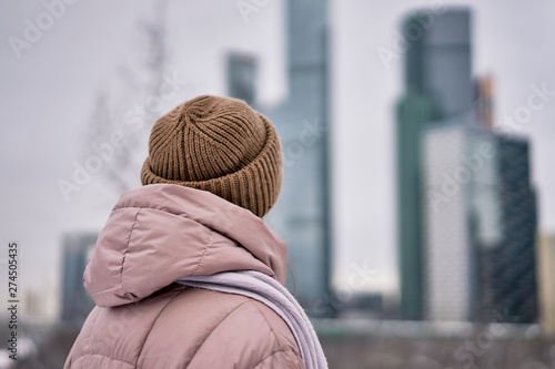 the girl in the hat looks at the city in winter, the view from the back