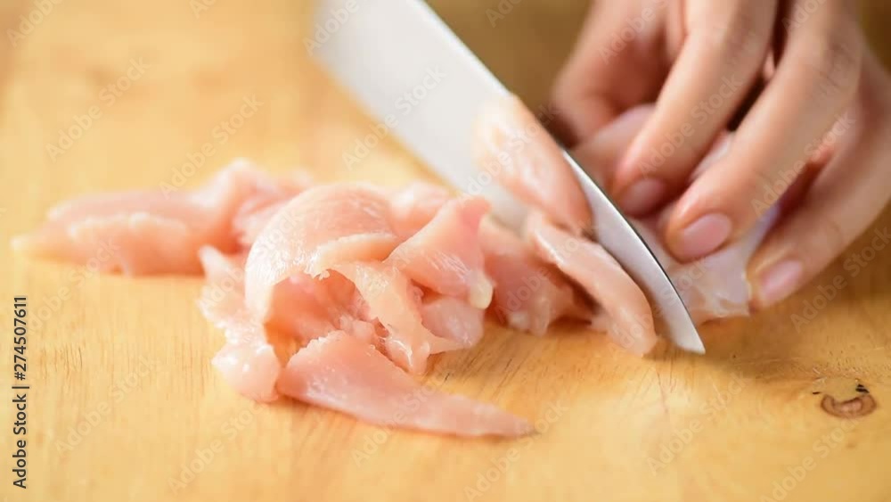 Hand holding knife and cutting chicken meat on wooden board for cooking Hand holding knife and cutting chicken meat on wooden board for cooking