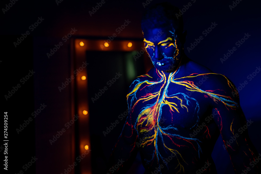 UV patterns body art of the circulatory system on a man's body. On the torso of a muscular athlete, veins and arteries are drawn with fluorescent dyes. Bodybuilder standing by the mirror with lamps. UV patterns body art of the circulatory system on a man's body. On the torso of a muscular athlete, veins and arteries are drawn with fluorescent dyes. Bodybuilder standing by the mirror with lamps.