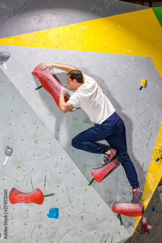 Rock climber man hanging on a bouldering climbing wall, inside on colored hooks