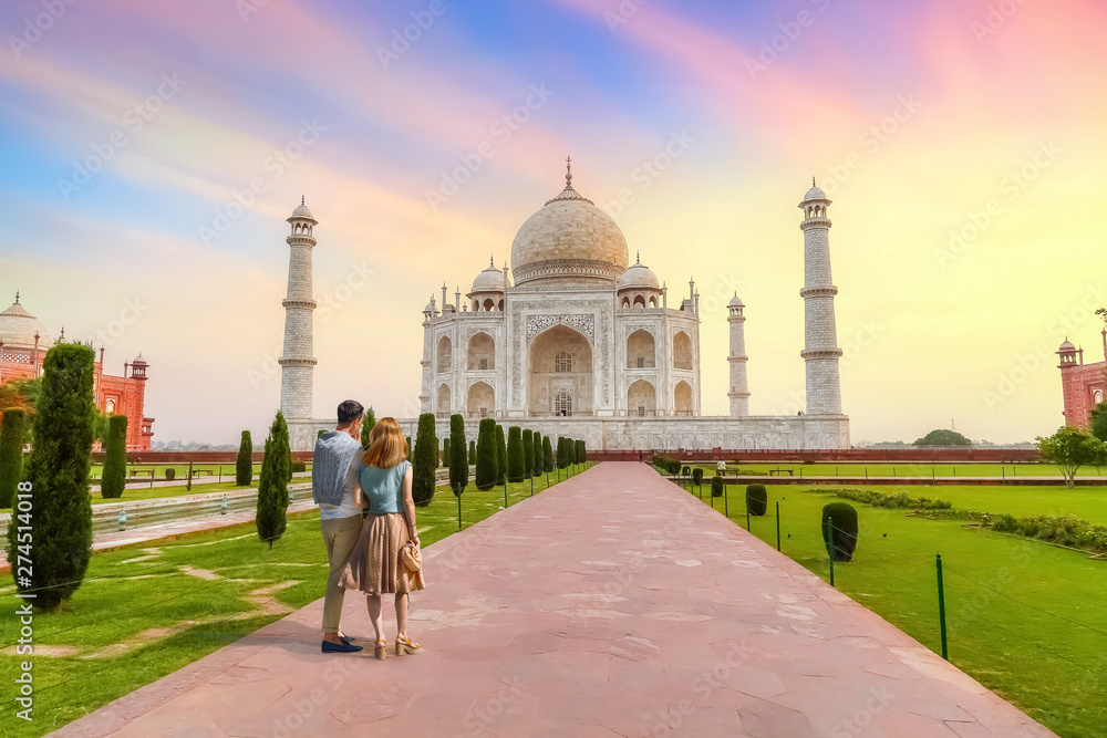 Taj Mahal white marble mausoleum at sunset with view of tourist couple enjoying the sunrise view at Agra, India