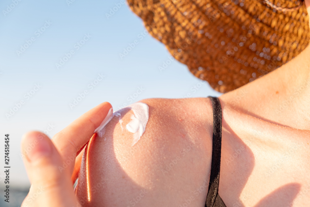 Fototapeta premium Applying suntan cream on the beach. UV or sun radiation protect concept: woman uses protective cream at the seaside, close-up view