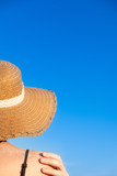 Summer holidays mood: female in beach hat, covered in sand in bright blue background. Shoulders of a young woman in a retro hat, chot from behind