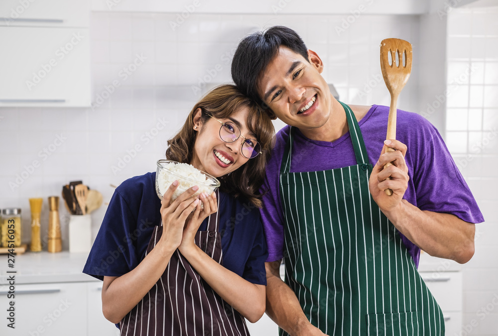 Smiling happy young Asian couple wearing apron and cooking together in ...